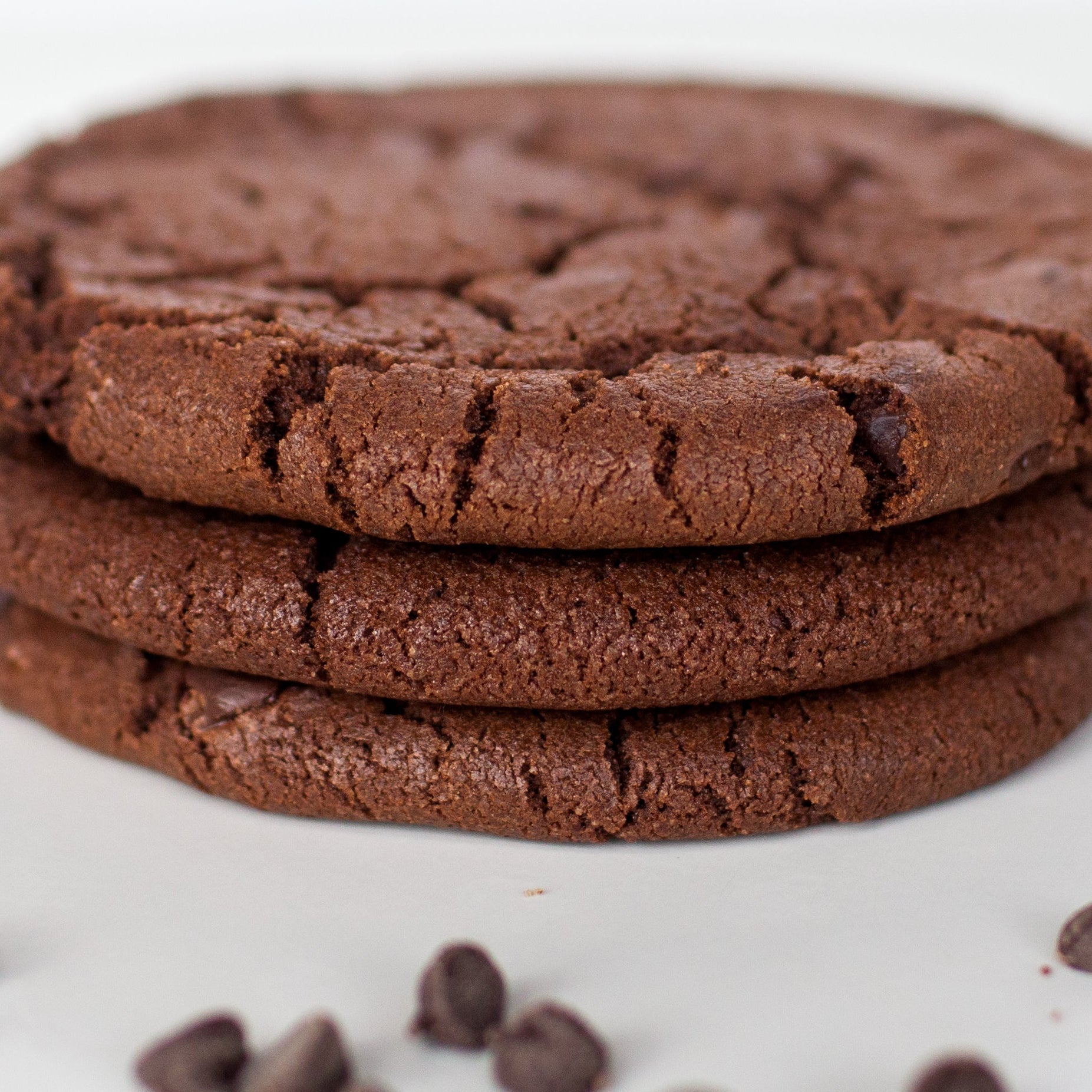 Stack of chocolate cookies with scattered chocolate chips on a white background