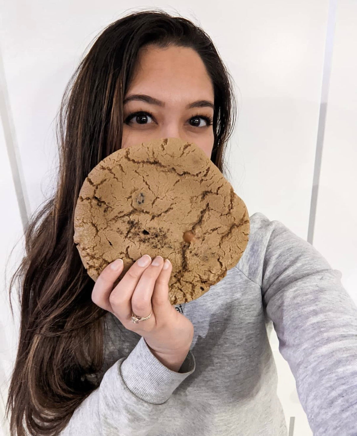 Person holding a large cookie in front of their face against a white background