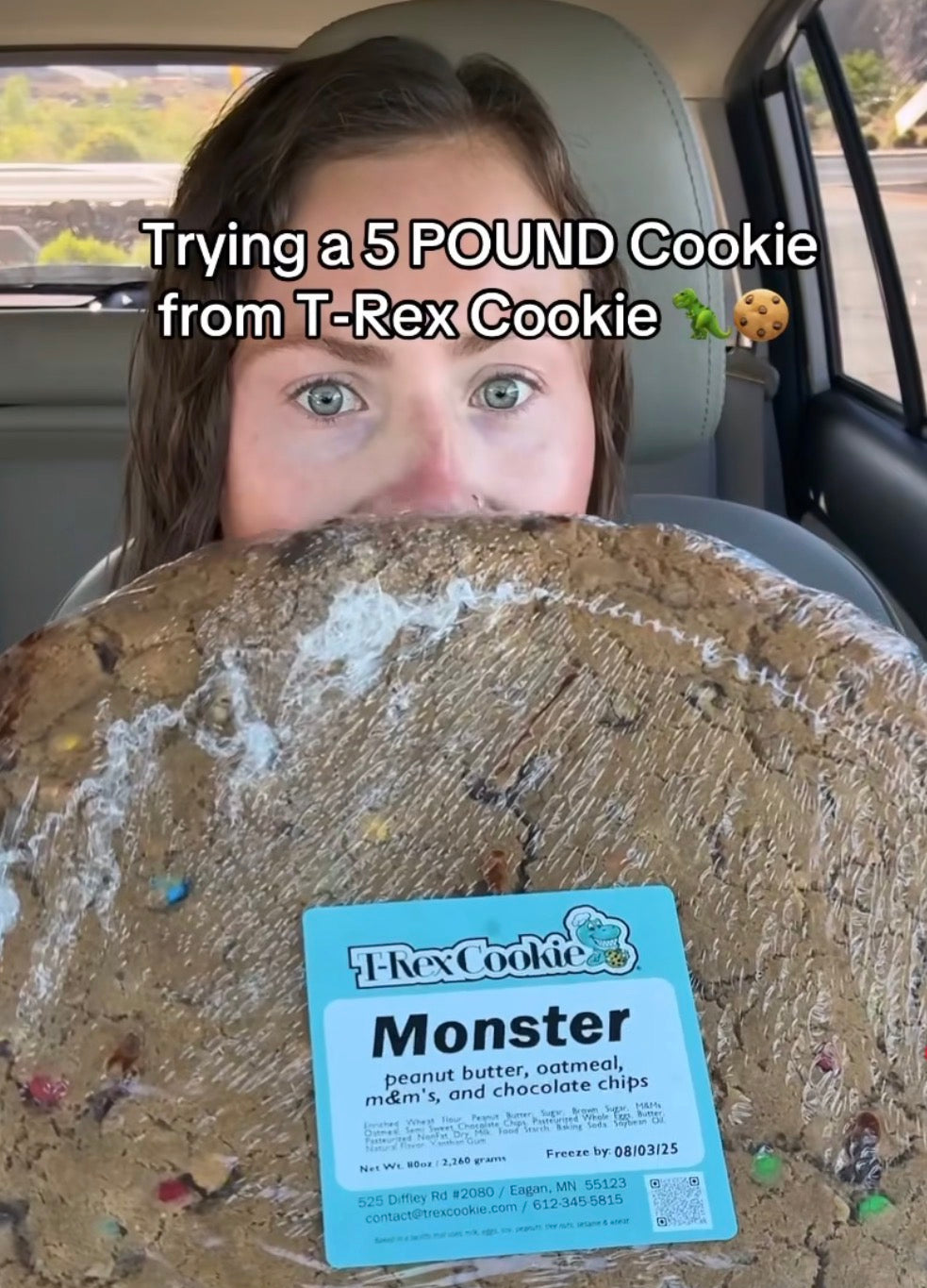 Person holding a large cookie labeled 'Monster' with text about trying a 5-pound cookie from T-Rex Cookie.