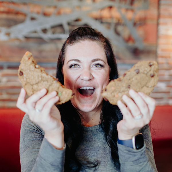 Woman holding two cookies up to her face with a smile in a casual setting